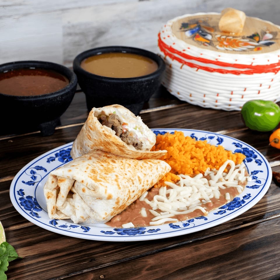 Two burritos with rice, beans, and cheese, alongside two bowls of salsa and a woven basket.