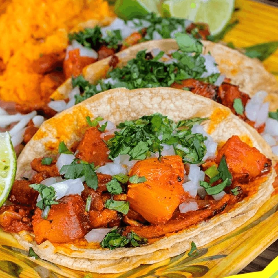 Three vibrant Tacos Don Misael al pastor tacos with cilantro, onions, and lime wedges.