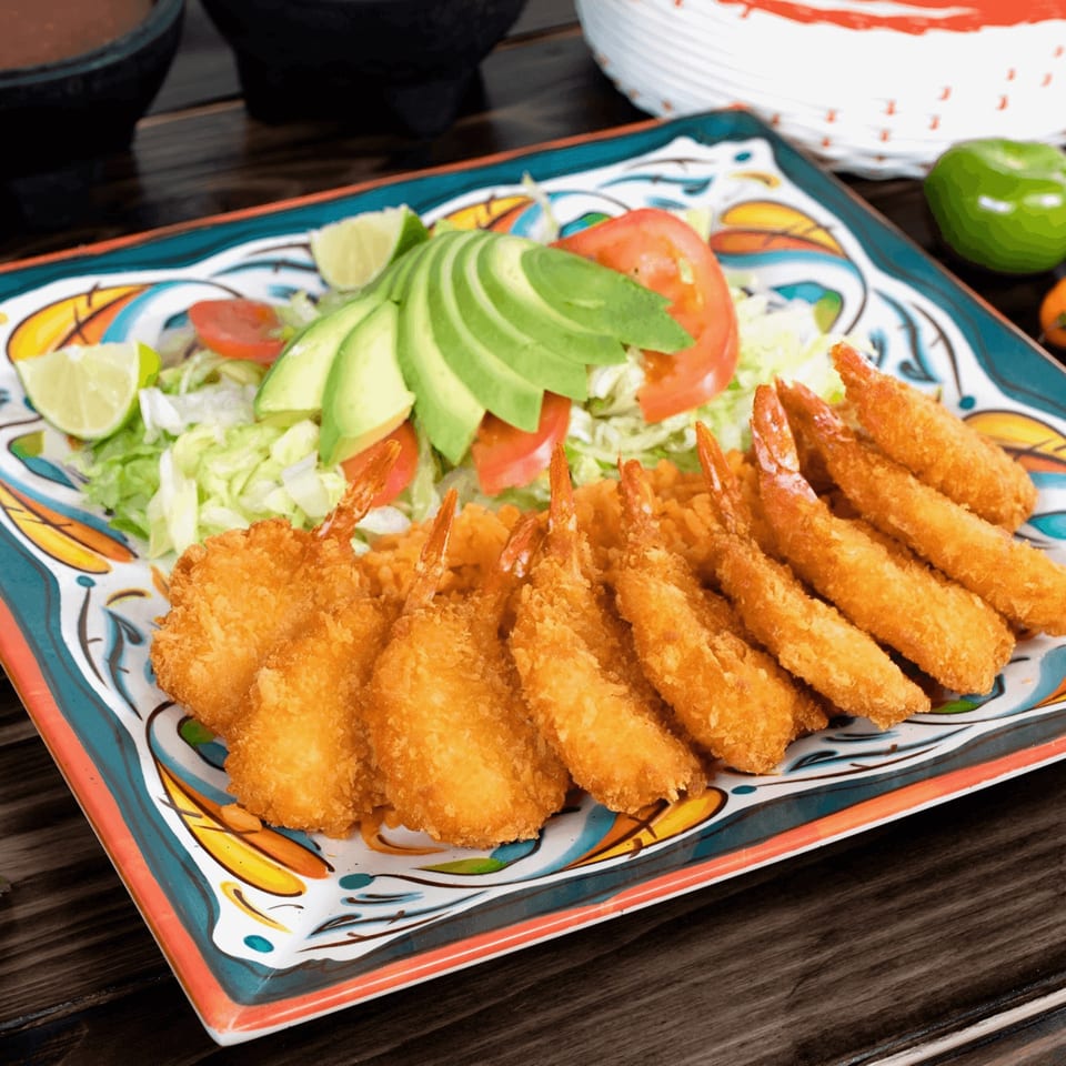 Crispy fried shrimp with rice, sliced avocado, tomatoes, and lettuce on a colorful Mexican plate.
